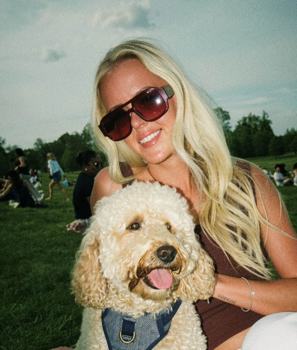 Ellie smiling with her cream labradoodle in a sunny park